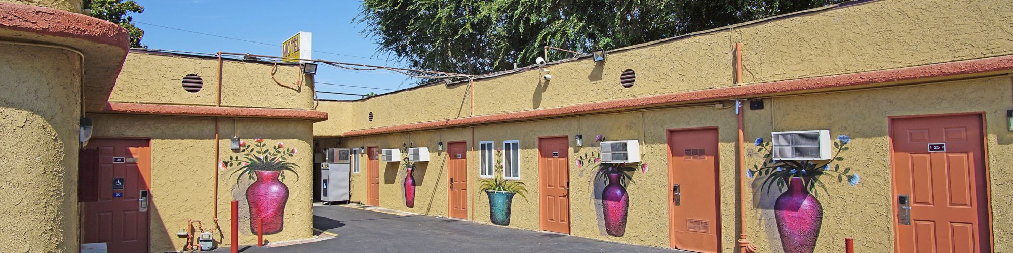 An outdoor area of a building with unit doors, wall air conditioners, and painted murals of pots and plants on the walls.