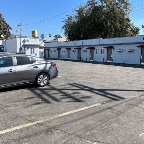 The image shows a parking lot with a parked car in front of a single-story motel or apartment building on a clear day.