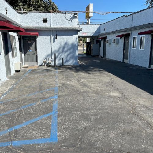 The image shows a motel courtyard with multiple doors, a designated parking area, and shadows from the buildings under a clear sky.