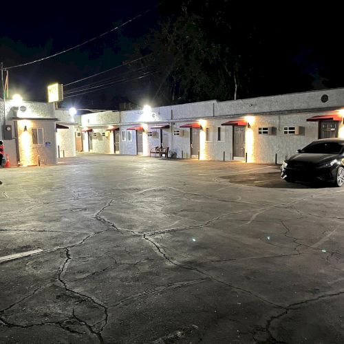 A nighttime image showing a small, well-lit motel parking lot with a couple of parked cars.