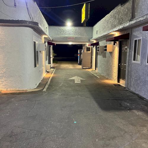 It's a dimly lit alley or passageway between buildings at night, featuring an arrow on the ground pointing forward.