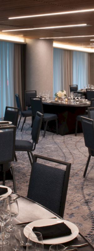 A banquet hall set up with round tables, each adorned with place settings, black napkins, and floral centerpieces, under modern lighting fixtures.