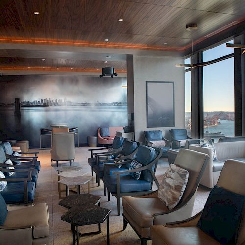 A modern lounge area with comfortable seating, large windows offering a scenic view, and a cityscape mural on one wall, ending the sentence.