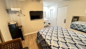 A hotel room with a bed, TV, mini-fridge, and open closet. There's a small bathroom visible through an open door.