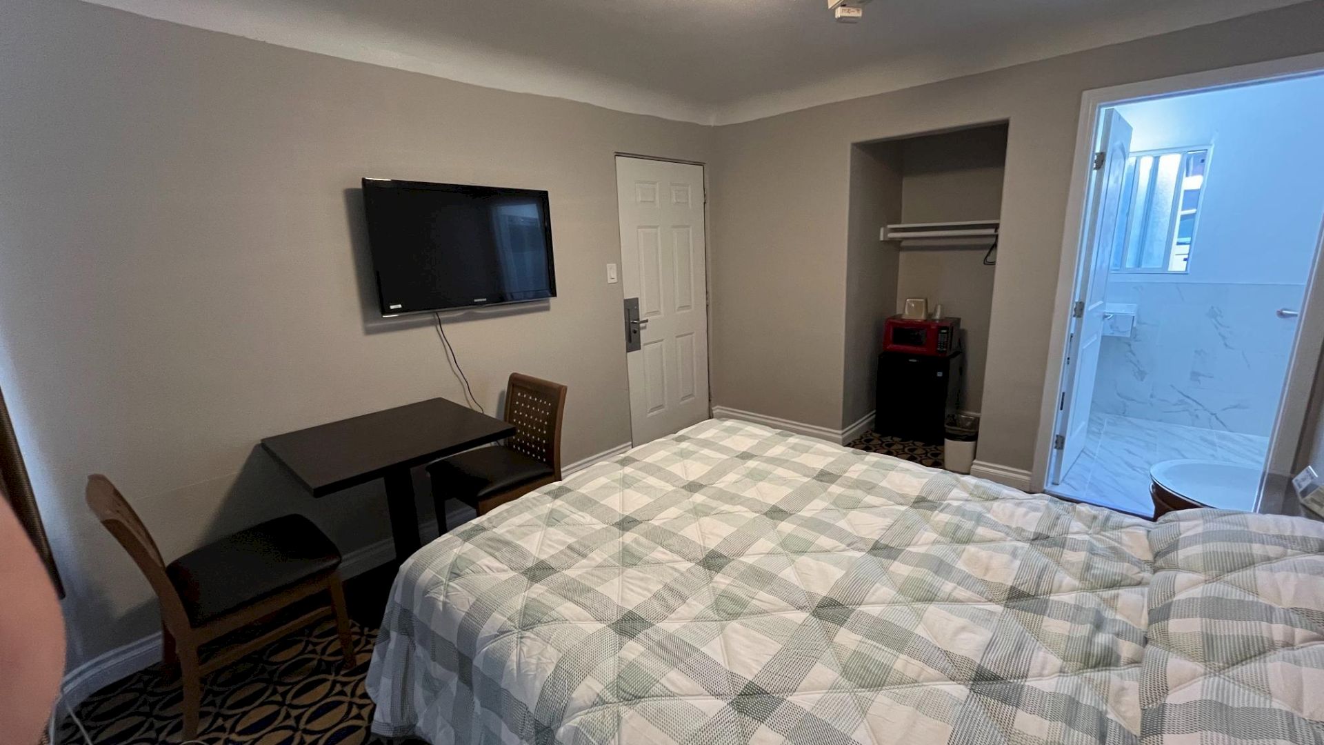 A hotel room with a bed, wall-mounted TV, table with chairs, open closet, and a view into a bathroom.