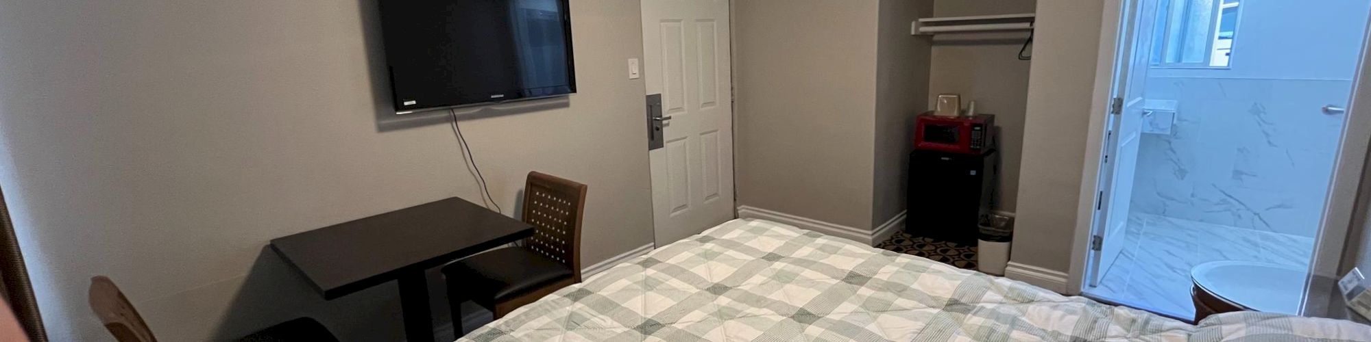 A hotel room with a bed, wall-mounted TV, table with chairs, open closet, and a view into a bathroom.